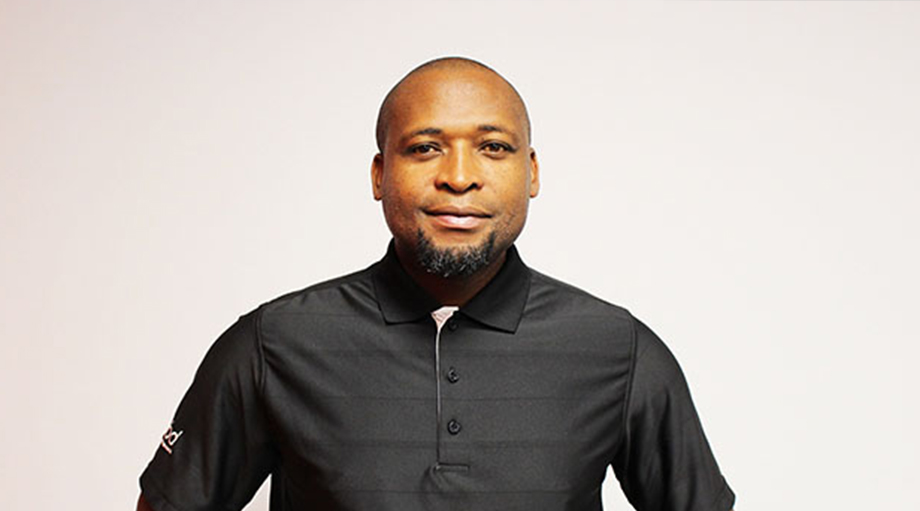 A man stands against a plain white background, wearing a black polo shirt.