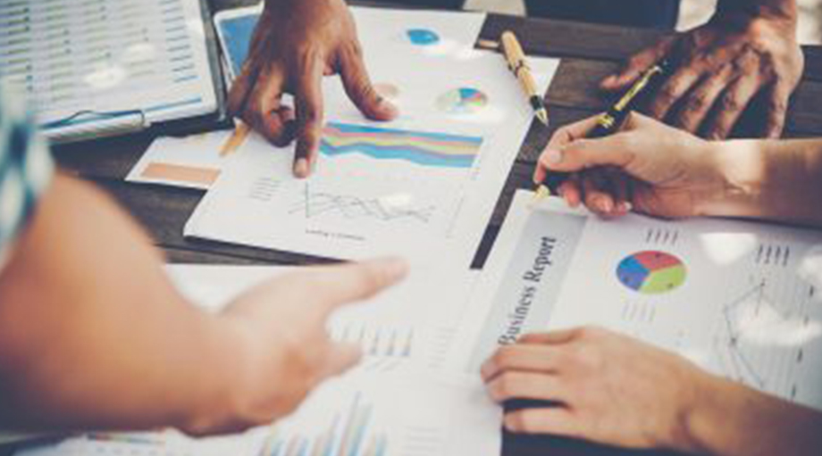 A group of people discussing colorful charts and graphs on business reports at a table, showing collaboration and analysis in a focused meeting.
