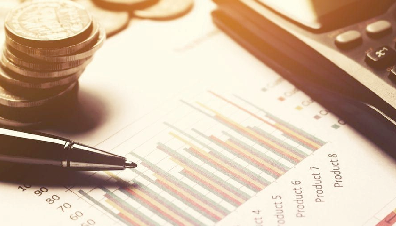 Coins stacked beside a pen, a colorful bar chart, and a calculator on a desk, suggesting financial analysis and planning in warm lighting.