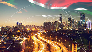 City skyline at dusk with illuminated highways and bright skyscrapers. Digital lines crisscross the sky, symbolizing connectivity.