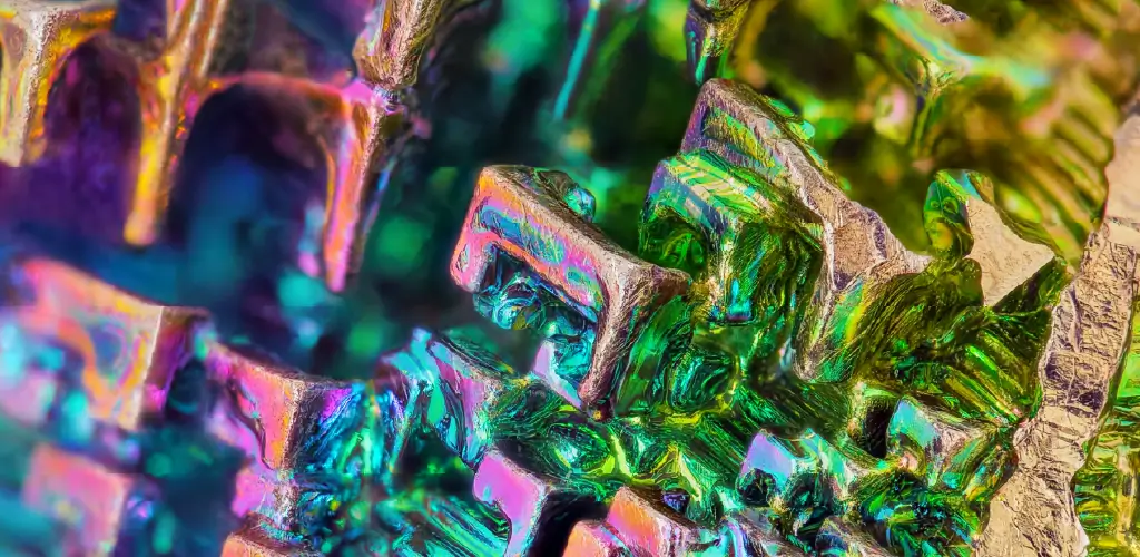 Close-up of a bismuth crystal showing its intricate geometric structure. Vivid iridescent colors of pink, blue, and green create a vibrant, mesmerizing effect.
