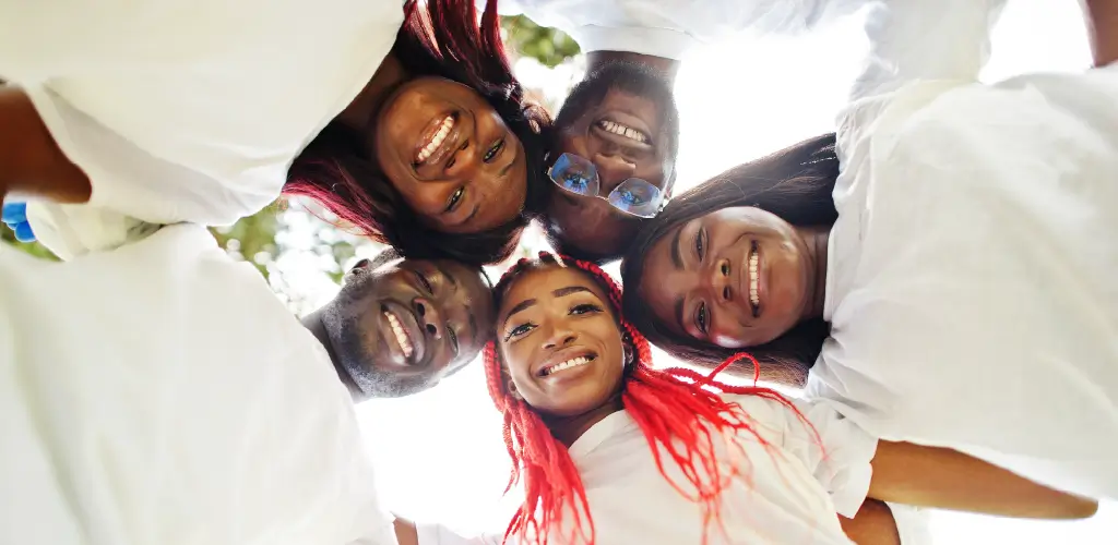 A joyful group of five people form a circle, looking down at the camera with bright smiles. They wear white shirts, conveying unity and happiness.