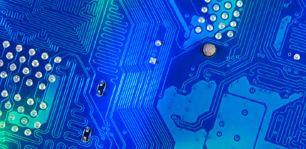 Close-up of a blue circuit board with intricate patterns, silver solder points, and reflective pathways. The image evokes a modern, technological feel.