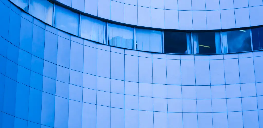 Curved blue-tinted glass facade with rectangular windows lined horizontally. The building reflects a modern, sleek, and minimalist architectural style.