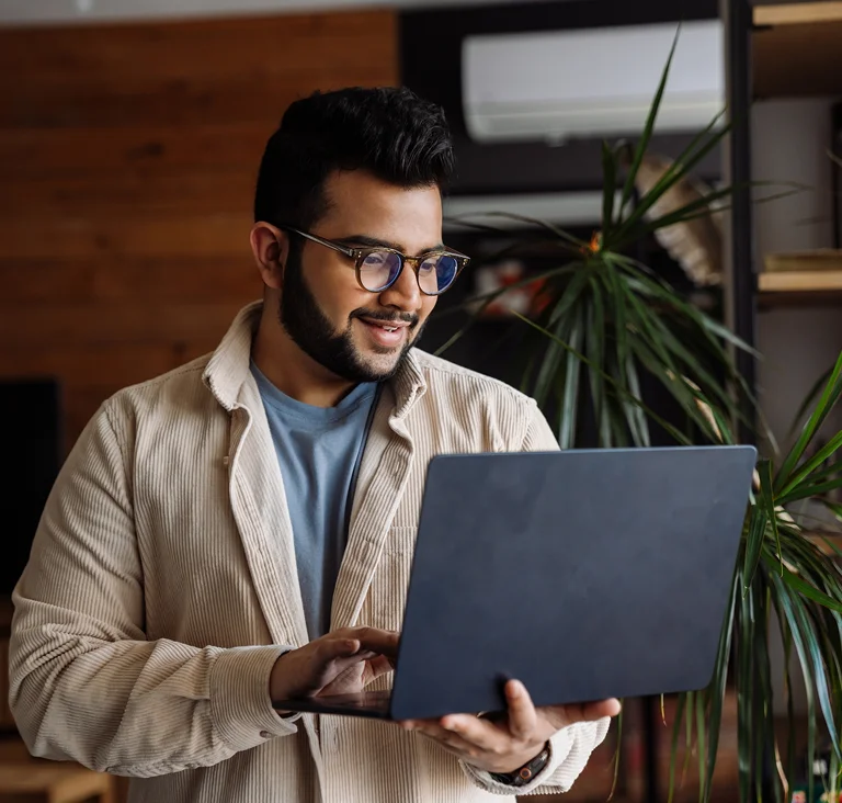 A man wearing glasses working on a laptop in a modern office, representing productivity and remote work.
