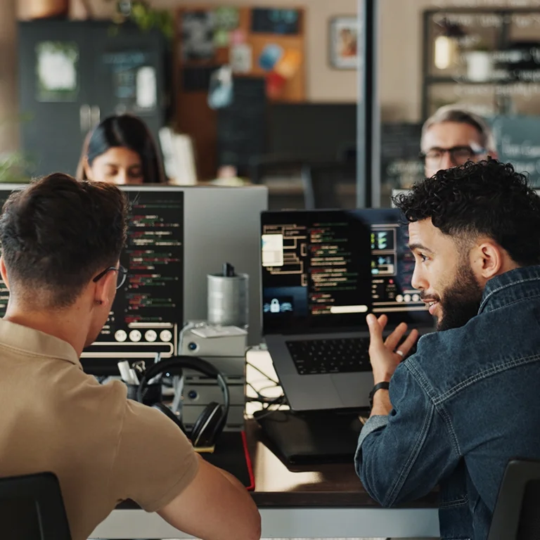 Two developers discussing code displayed on dual monitors in a modern office, representing cloud collaboration.