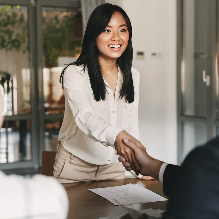 A woman shaking hands with a colleague in an office, symbolising partnership and client trust.