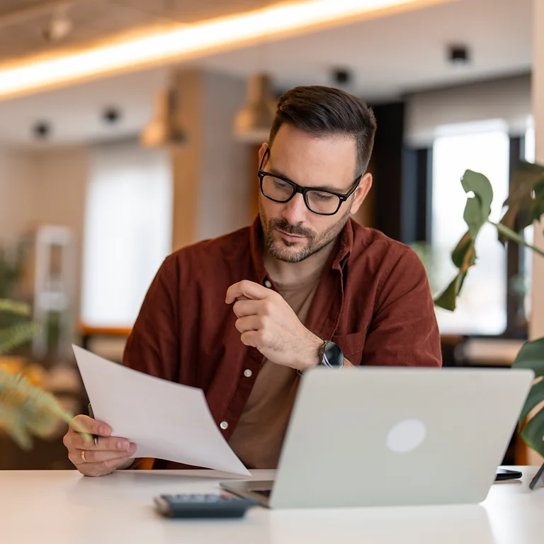 A man working thoughtfully at his laptop, reviewing a document, representing insurance analysis and focus.
