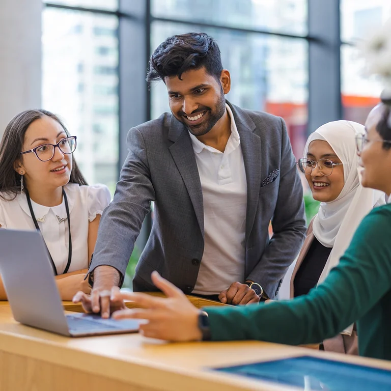 A diverse team gathered around a laptop discussing a project, representing collaborative software testing.