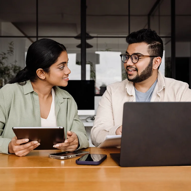 Two professionals discussing a project at a desk with laptops, representing teamwork in UX design.