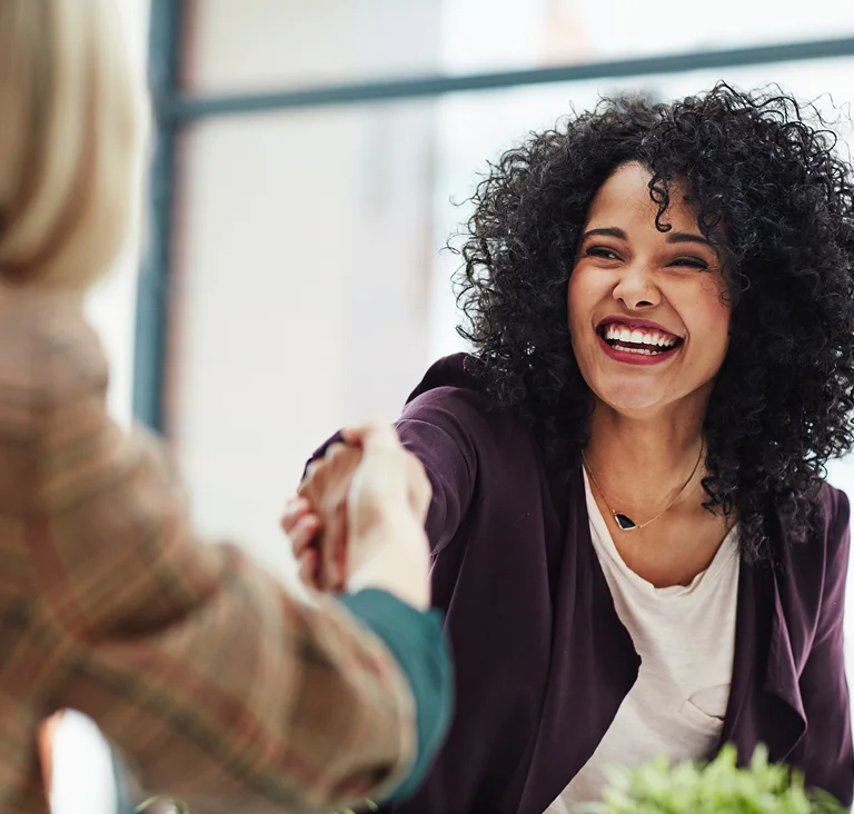 A smiling woman with curly hair shaking hands in an office, symbolising trust and successful collaboration.