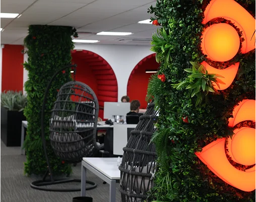 A modern office space with greenery, hanging chairs, and illuminated company branding, symbolising a creative workplace.