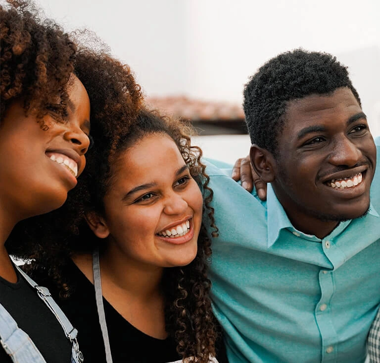 Three friends smile warmly in a close embrace. They appear joyful and relaxed against a soft, blurred background, conveying a sense of unity and happiness.