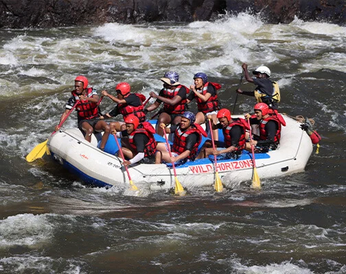 A group in helmets and life jackets navigates rough whitewater rapids in a raft, paddling vigorously with yellow oars, conveying excitement and teamwork.