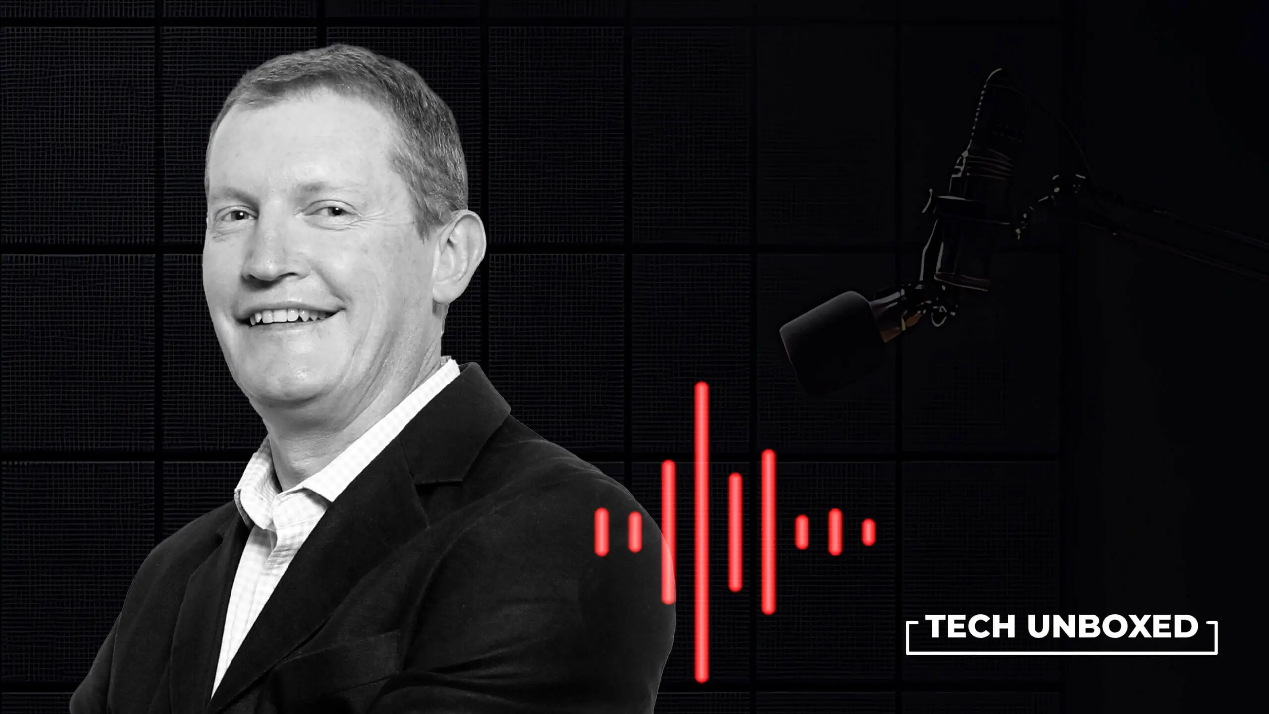 Smiling man in a suit on a podcast set with a microphone and sound waves.