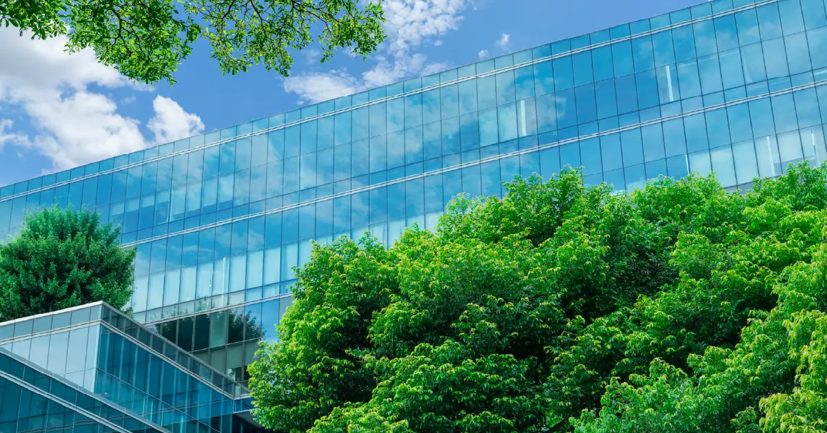 Secure by Design: Modern glass office building reflecting the blue sky, surrounded by lush green trees.